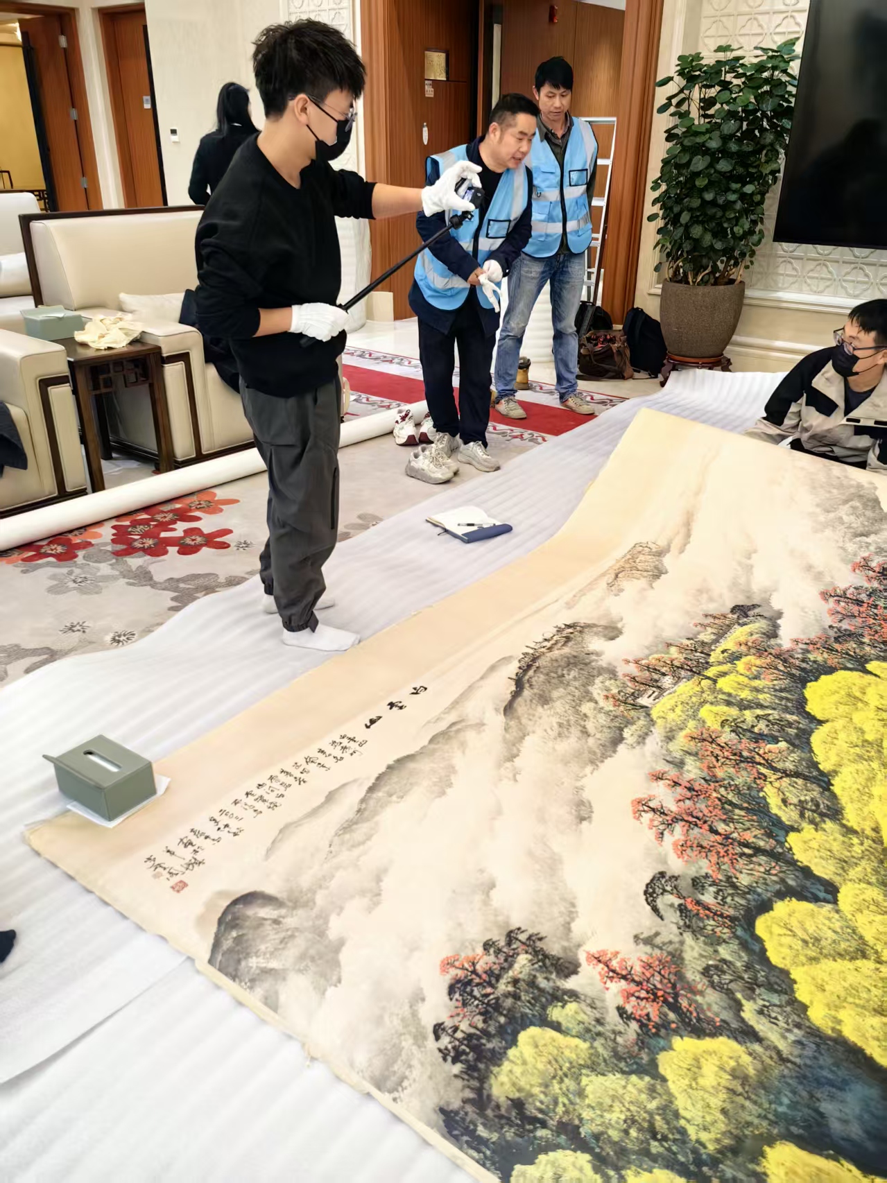 大幅卷轴平铺在专用缓冲毯上操作,避免弯折,多人协同平整转运